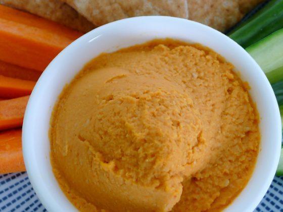 white bowl of red pepper hummus and carrot + cucumber sticks