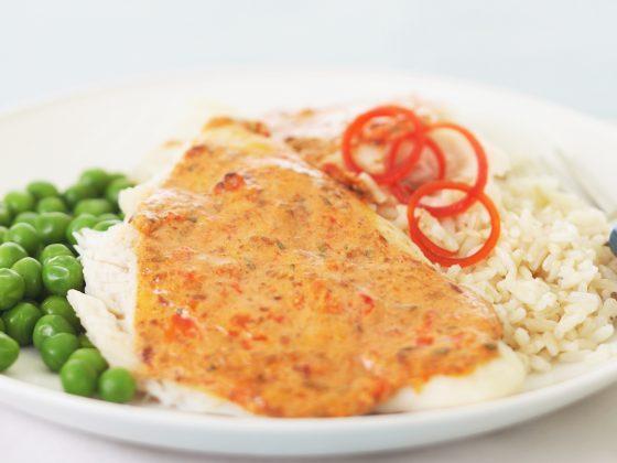 red pepper fish filet with rice and peas on white plate
