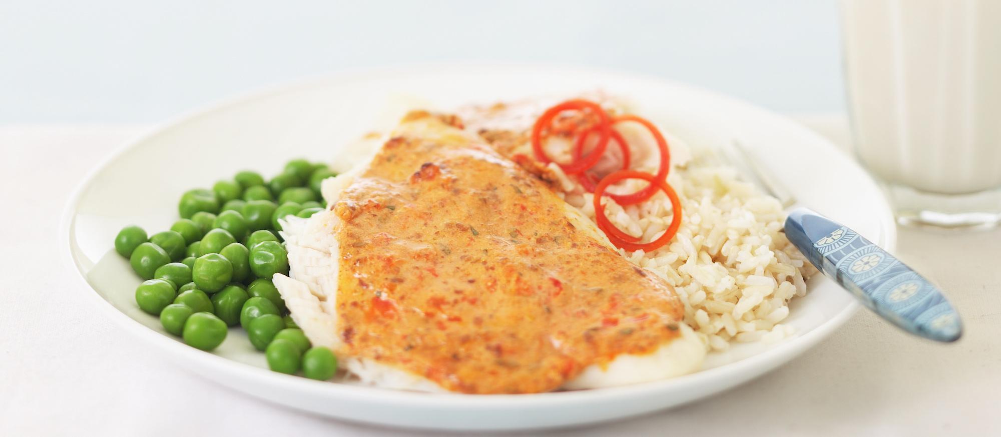 red pepper fish filet with rice and peas on white plate