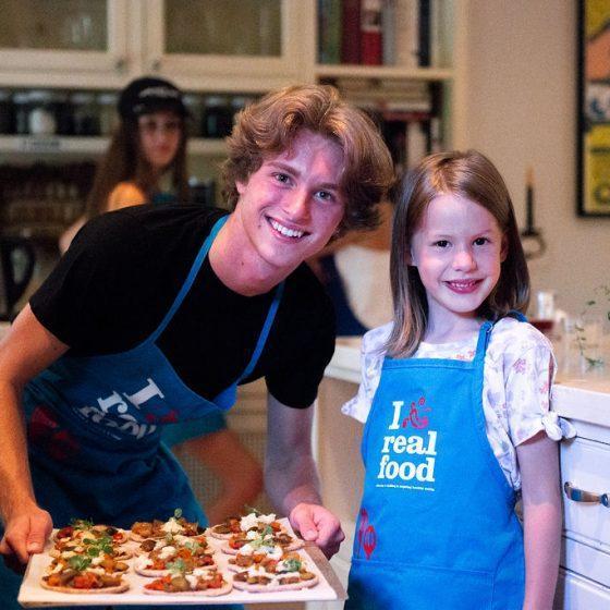 teenage boy with tray of food, with young girl, both wearing blue aprons
