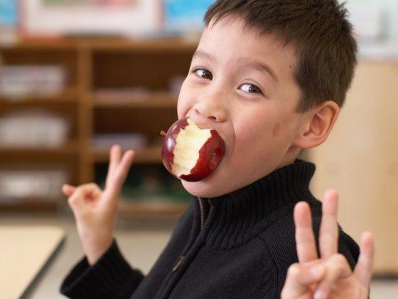 young boy in classroom with apple in mouth