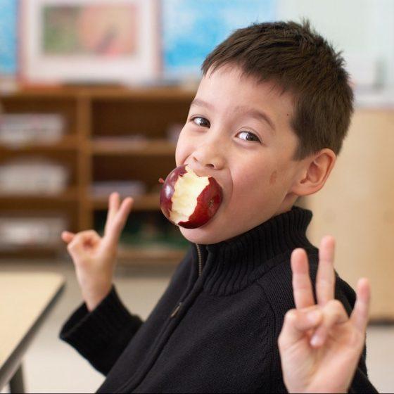 young boy in classroom with apple in mouth