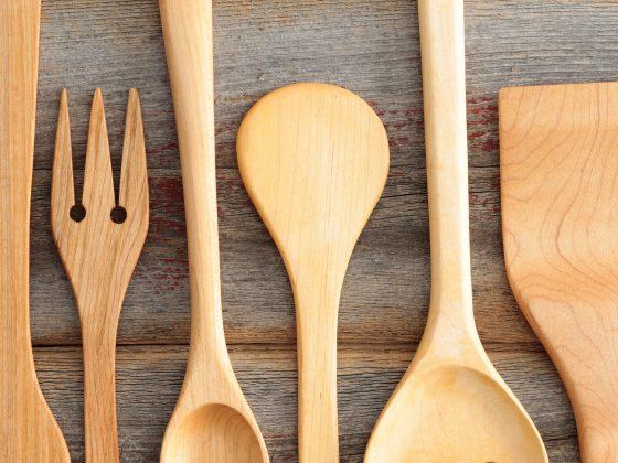 Set of rustic wooden handcrafted kitchen utensils with a spaghetti strainer, spoons , spatula and salad servers arranged in an alternating row on old wooden boards, view from above