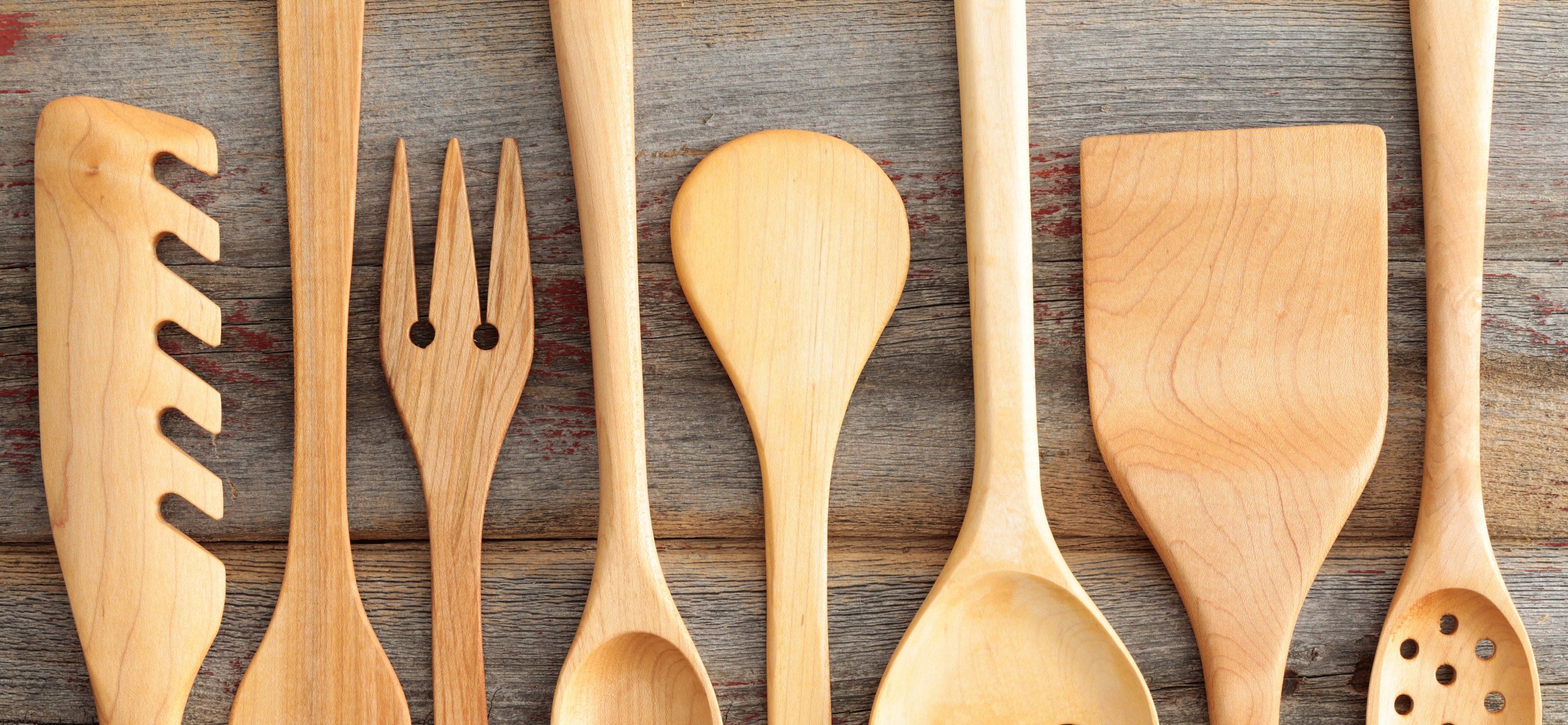 Set of rustic wooden handcrafted kitchen utensils with a spaghetti strainer, spoons , spatula and salad servers arranged in an alternating row on old wooden boards, view from above
