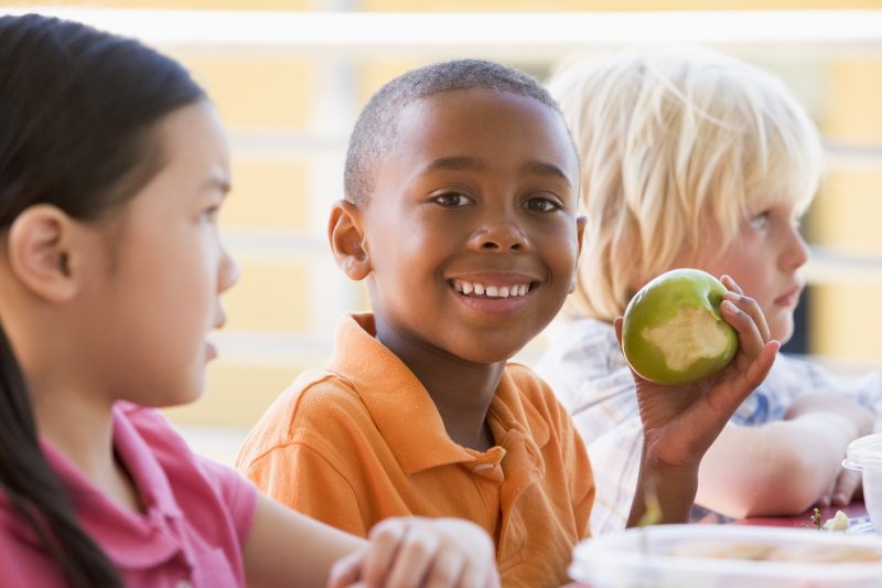 young boy smiling eating apple with peers