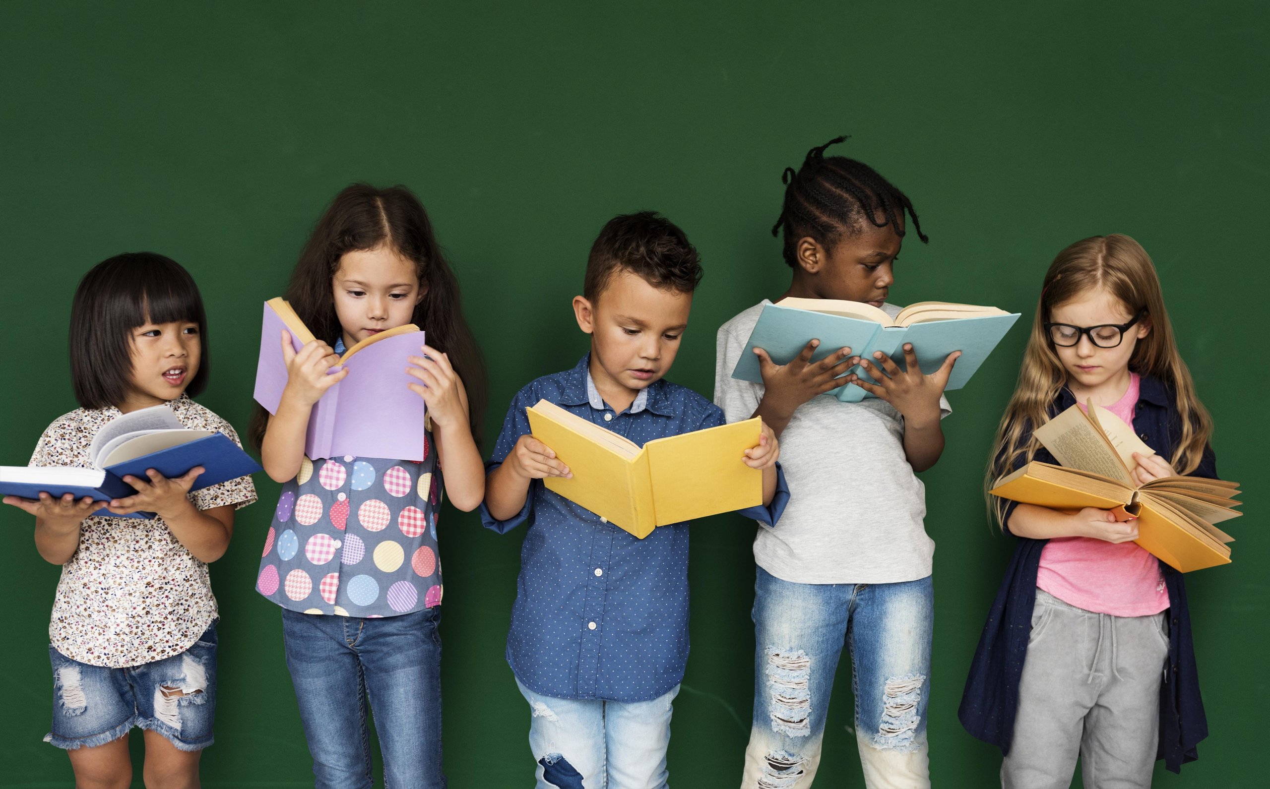 Group of school kids reading for education in front of dark green wall