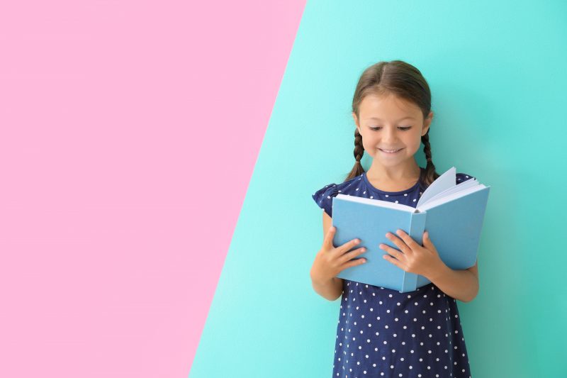Cute little girl reading book on pink and turquoise background