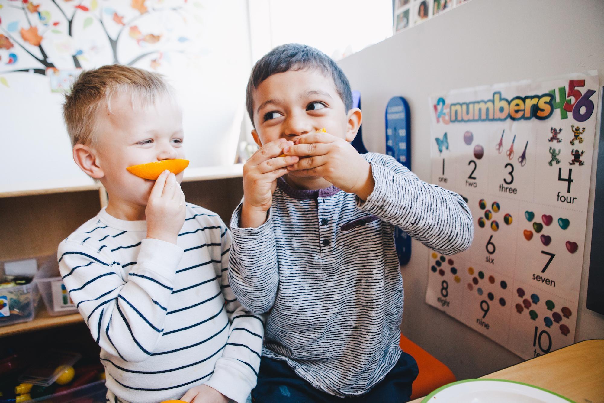 2 young boys in daycare eating orange slices