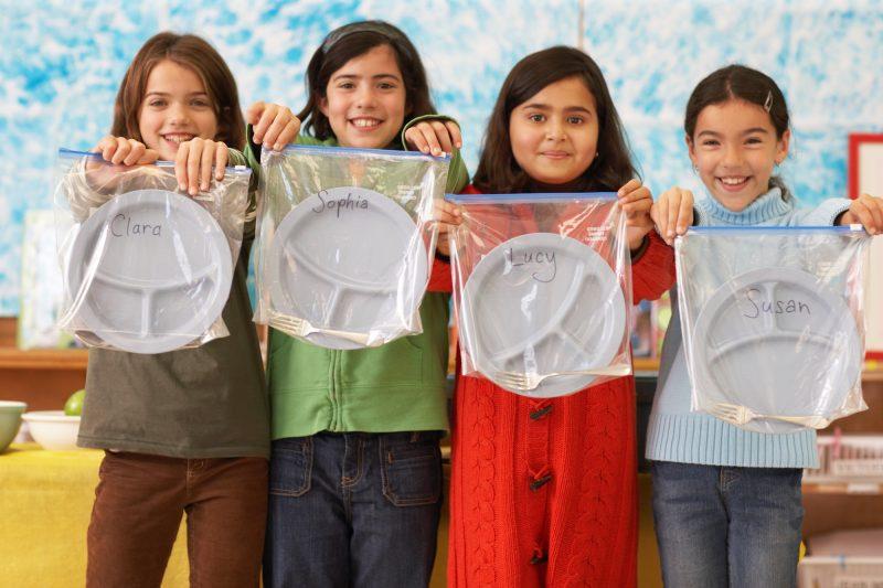 row of 4 school age girls holding divided plate in ziplock bags