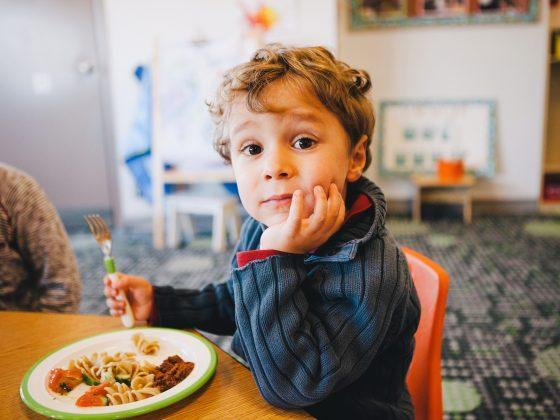 young boy at table with pasta salad in day care