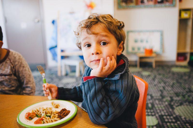 young boy at table with pasta salad in day care