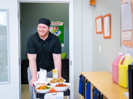 man in black shirt pushing food cart into classroom
