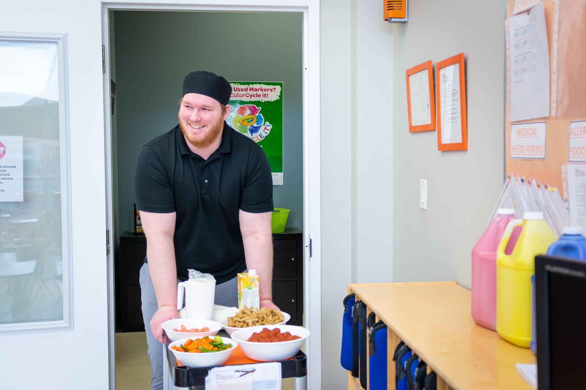 man in black shirt pushing food cart into classroom