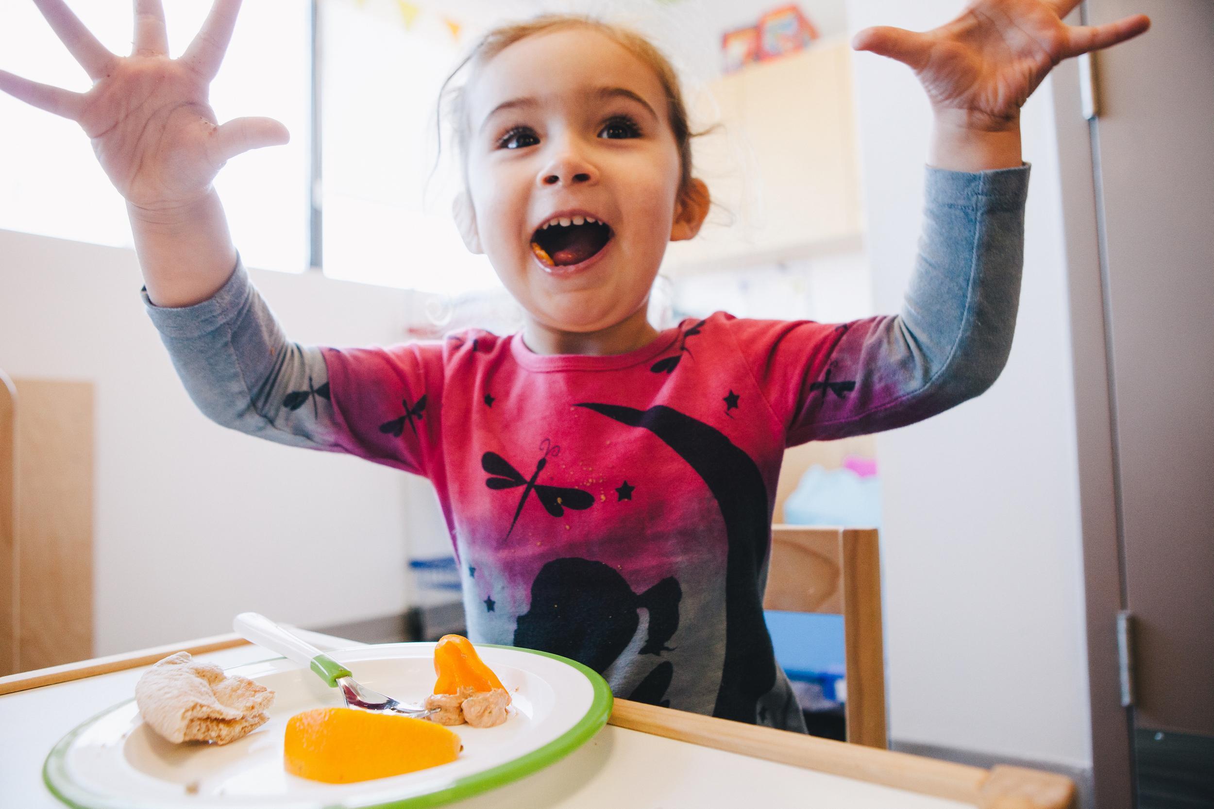 young girl with plate of food at table being expressive with hands