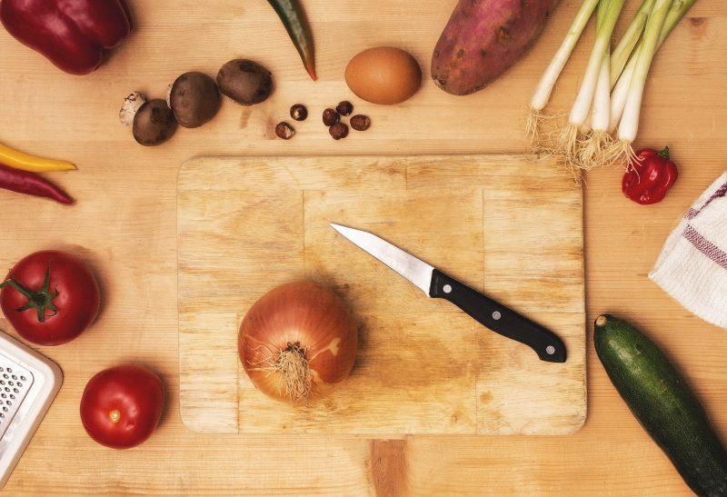 wood chopping board on wood table with onion and other vegetables