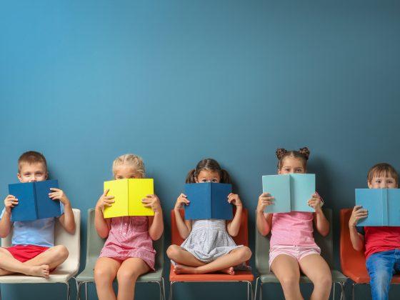 Cute little children reading books while sitting near blue wall