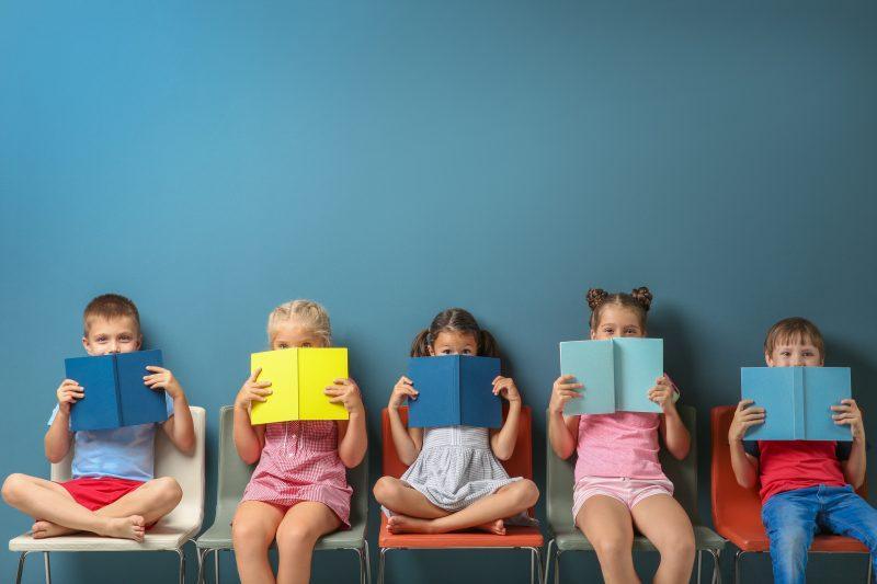 Cute little children reading books while sitting near blue wall