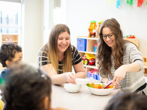 2 women ECEs serving salad in daycare class
