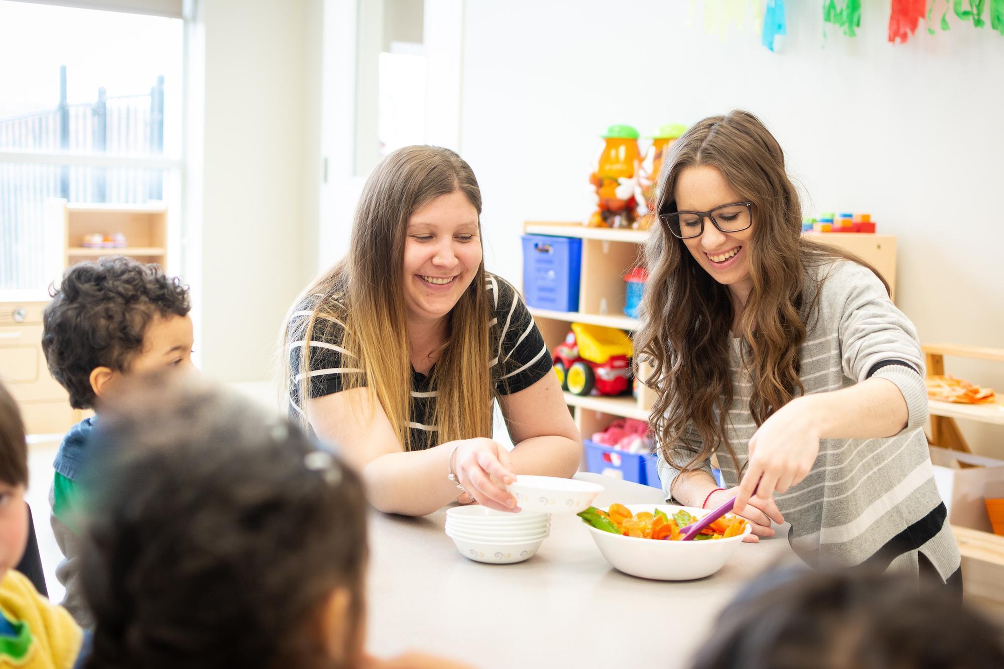 2 women ECEs serving salad in daycare class