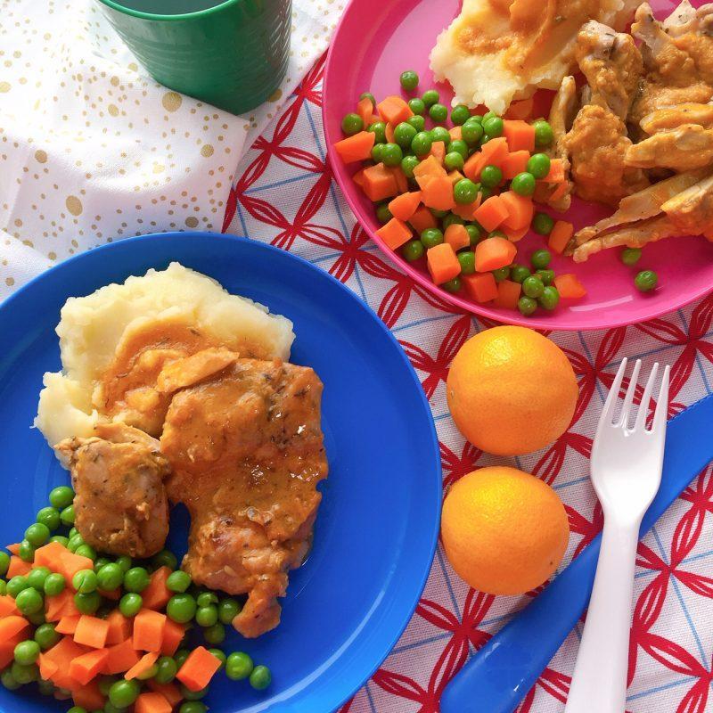 blue and pink plates of peas & carrots with mashed potatoes and chicken with gravy, 2 clementines