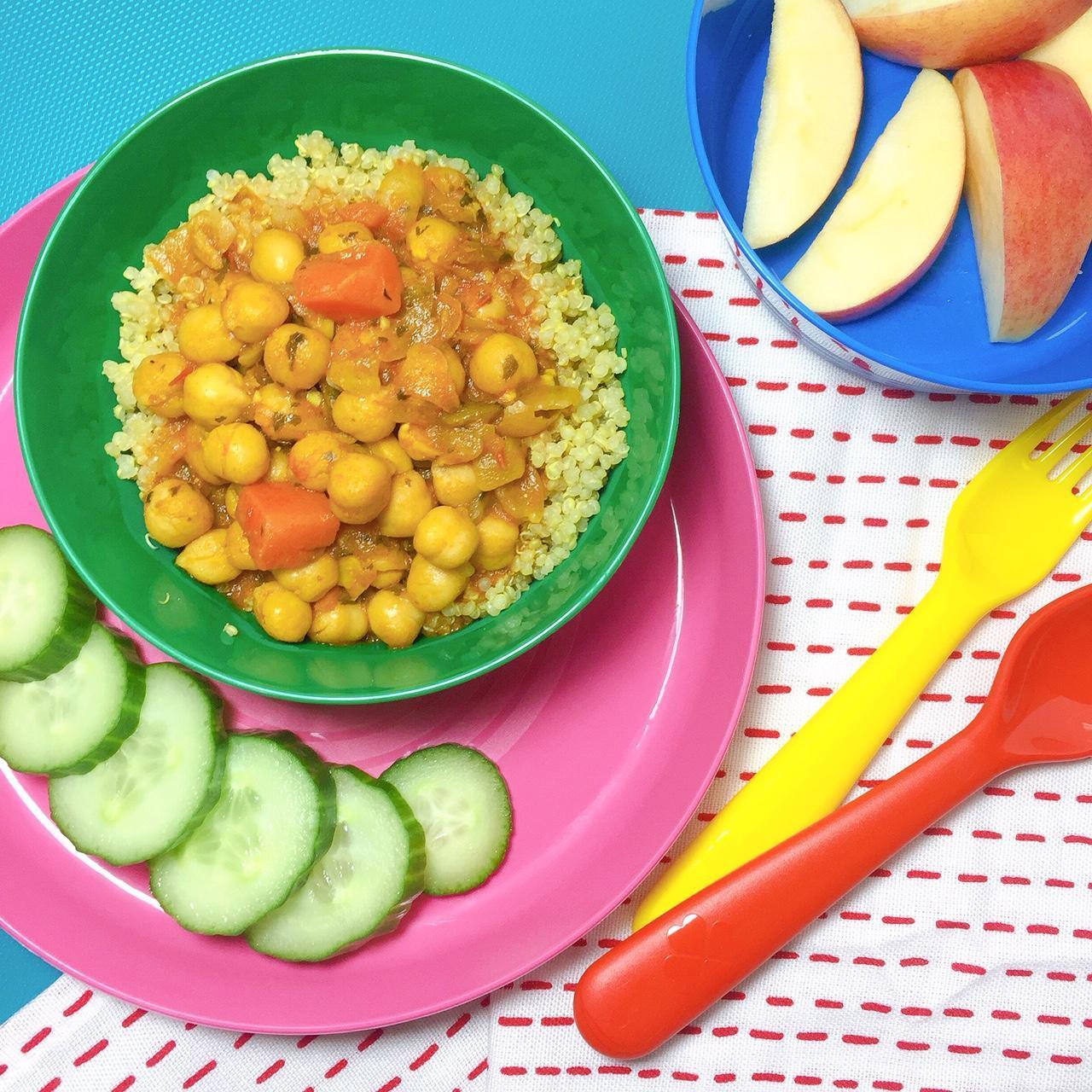 pink plate with cucumber slices with green bowl of chickpea chowder on top of quinoa, apples slices in background