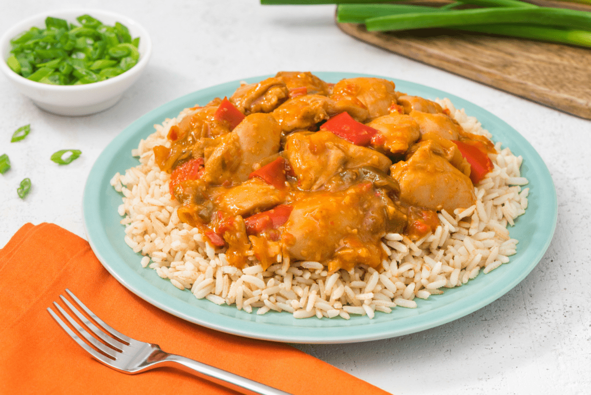 honouring children’s mental health week 4 table set with gong bao chicken and brown rice with a blue plate, silver fork and orange napkin