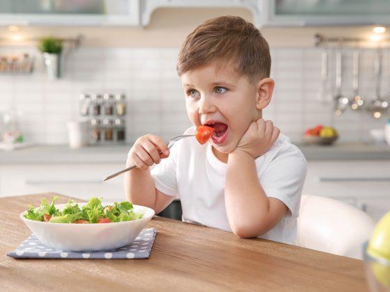 Adorable little boy eating vegetable salad at table in kitchen