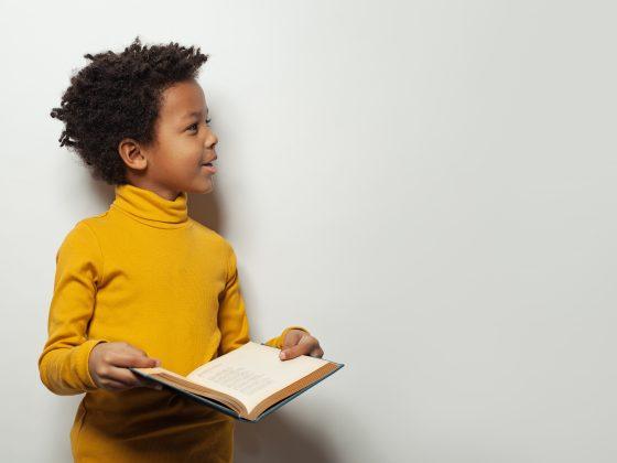 Curious black child boy reading a book on white background
