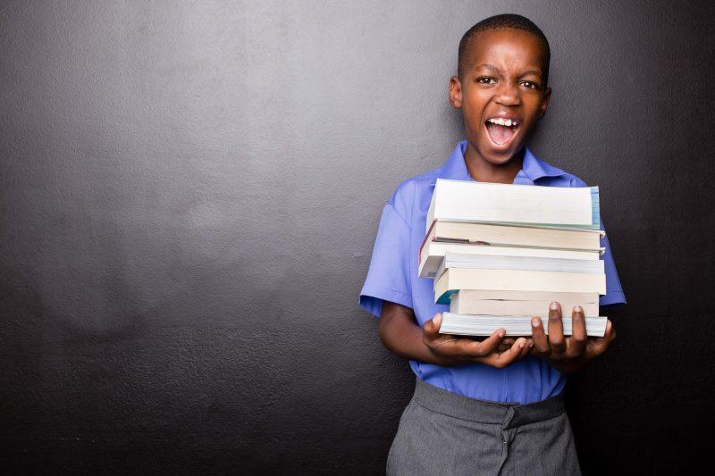 Young atractive black boy wearing school unifor while holding his school books and a green apple, looking excited about going back to school. looking excited about going back to school.