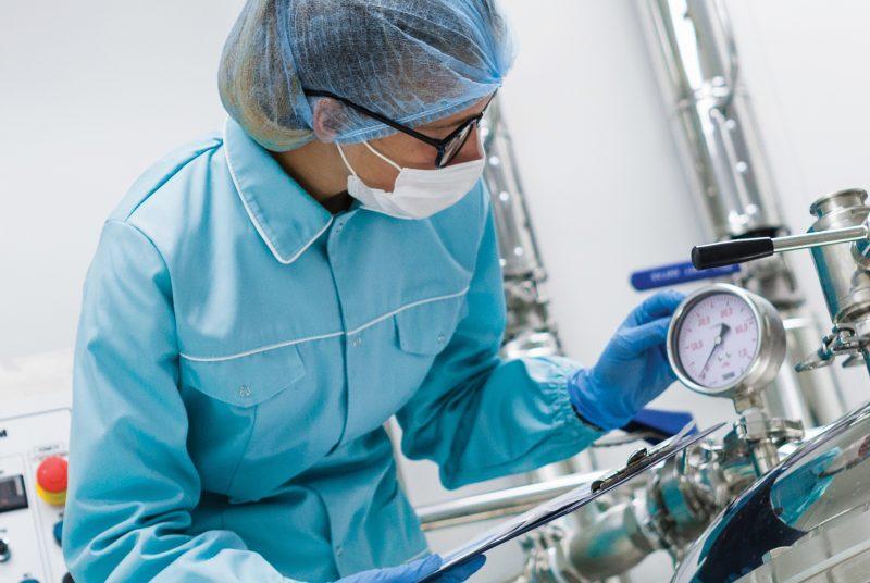 lab tech woman wearing glasses, mask, hairnet, blue jacket with clipboard