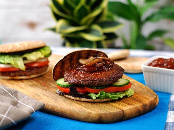 beef & mushroom burger with lettuce tomato and cucumber on wood board, ketchup in background