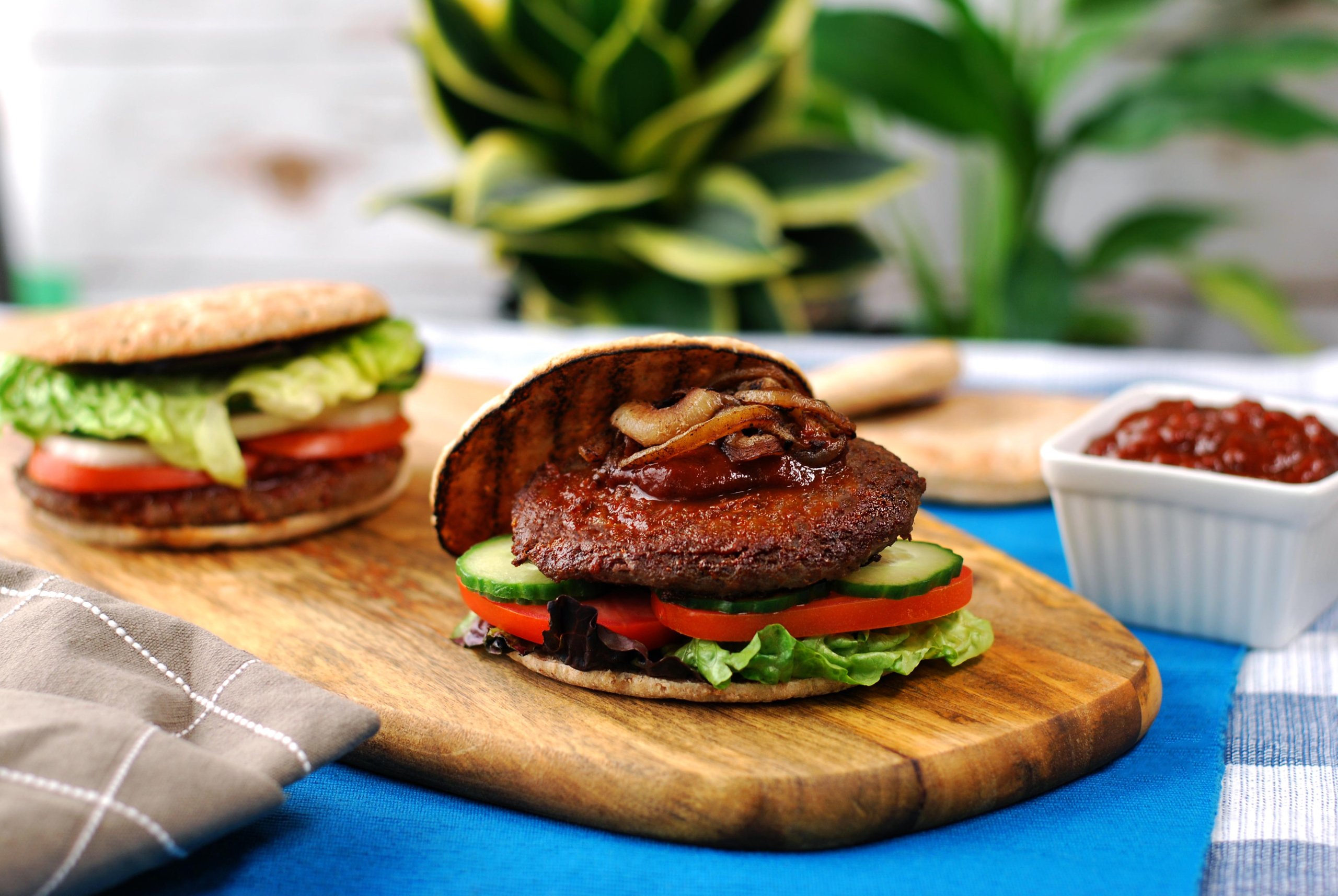 beef & mushroom burger with lettuce tomato and cucumber on wood board, ketchup in background