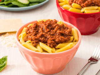 a pink bowl full of penne pasta features a delicious pile of beef bolognese made with ontario grass-fed, pasture raised beef without added hormones or routine antibiotics made by Real Food for Real Kids for their child care catering service