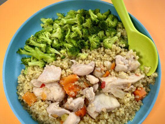 kids meal of organic chicken fricassee with quinoa and broccoli on a blue plate and orange mat and green spoon