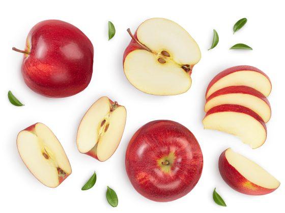 white background with an array of red apples, some sliced, some quartered. a few scattered green leaves surround them