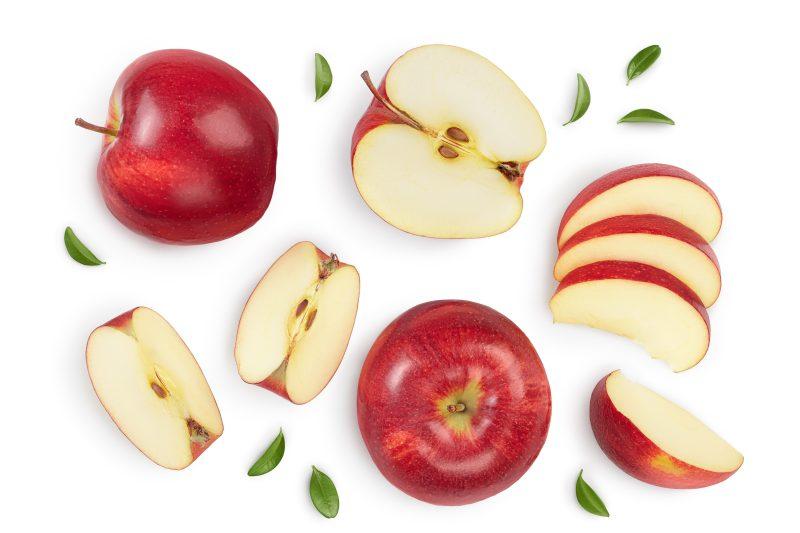 white background with an array of red apples, some sliced, some quartered. a few scattered green leaves surround them