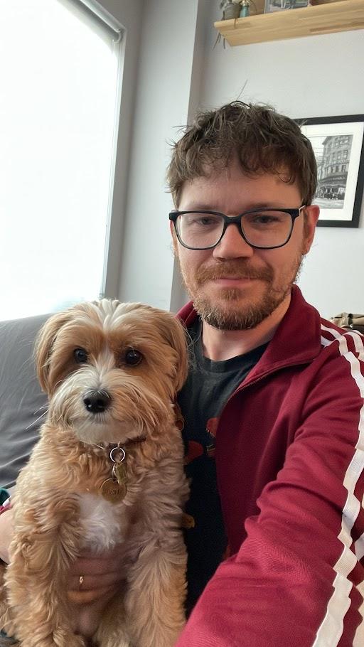Man with glasses and red jacket poses with his dog