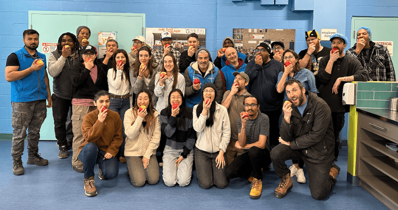 large group of staff members posing and biting into an apple together for the Great Big Crunch