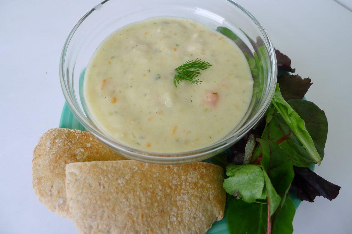 bowl of new england clam chowder in a clear glass bowl served with salad and bread