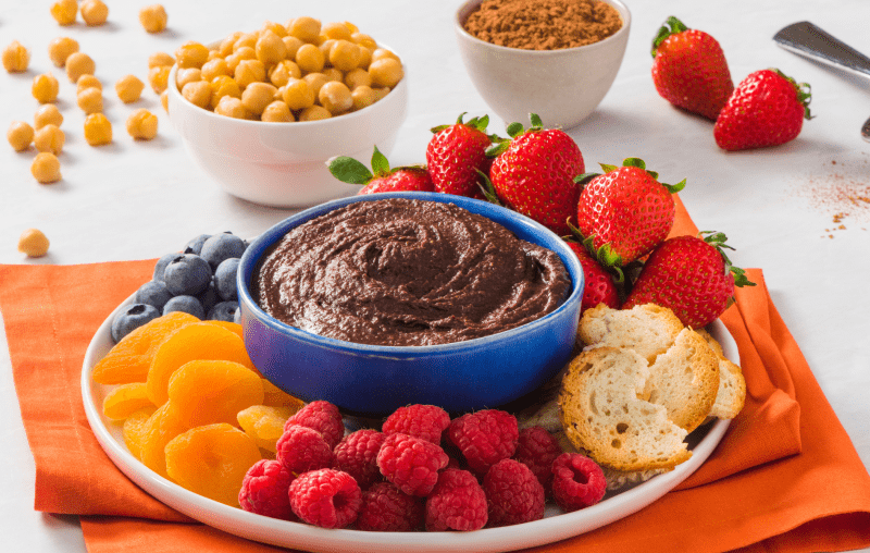 bowl of chocolate hummus, cocoa chic'pea spreadm, surrounded fruit