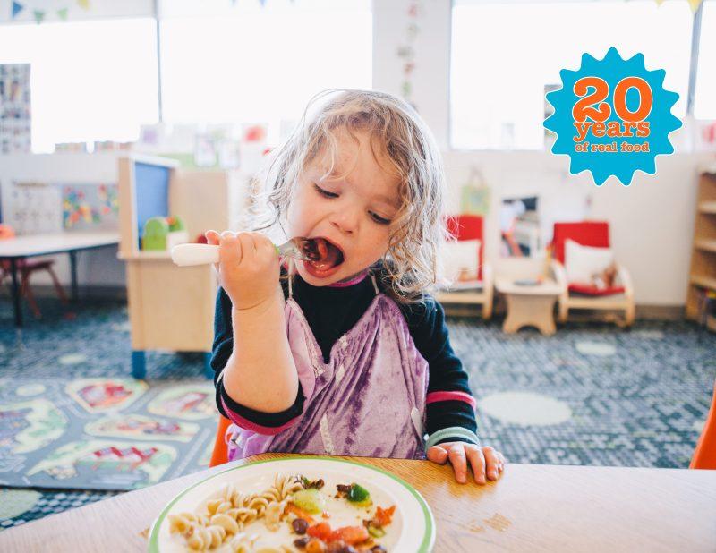 little girl with blonde hair happily eating lunch at child care