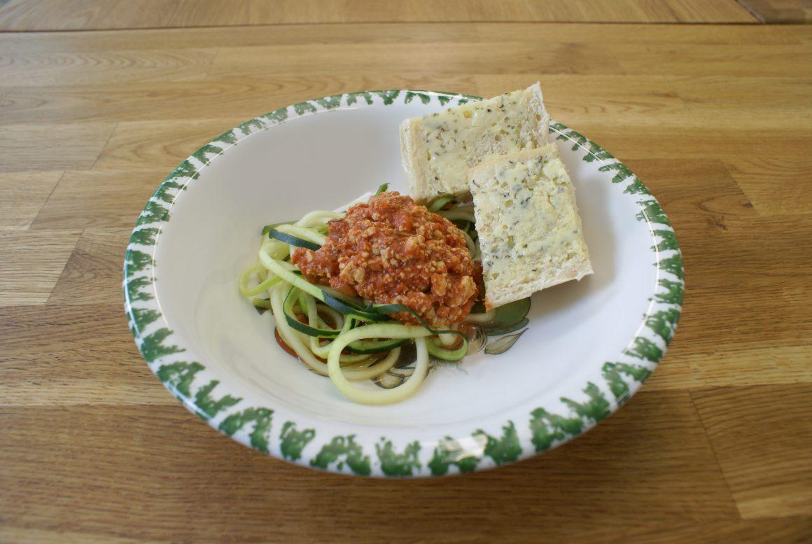 tofu bolognese, zucchini noodles, buttered bread on white and green plate