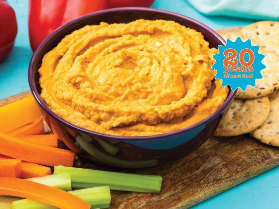 bowl of red pepper hummus with carrot & celery sticks and crackers on the side