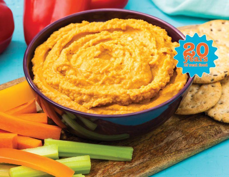 bowl of red pepper hummus with carrot & celery sticks and crackers on the side