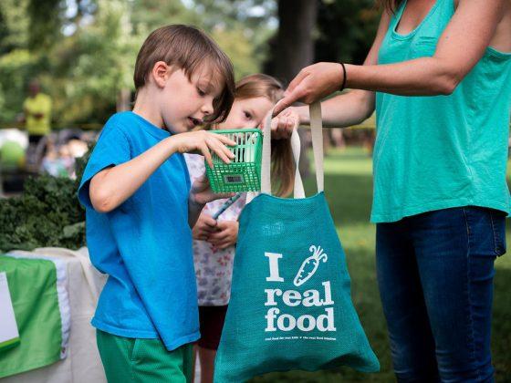 parent and child at local farmers market for local food week holding a "I love real food"