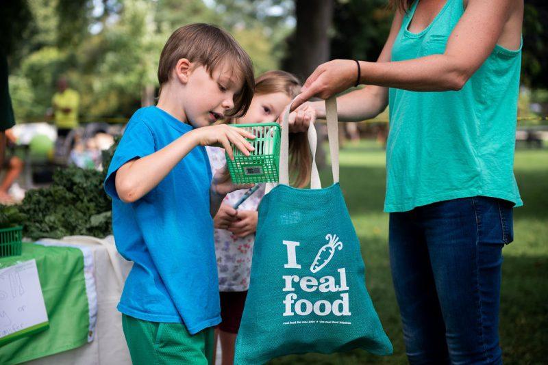 parent and child at local farmers market for local food week holding a "I love real food"