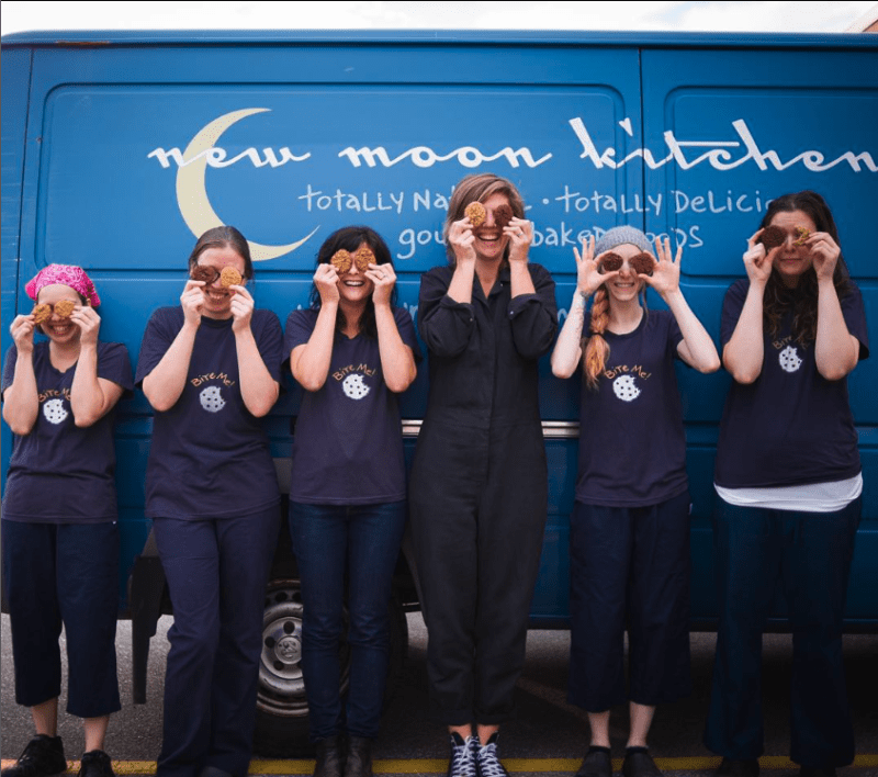 6 women standing in front of New Moon Kitchen van having fun smiling for photo