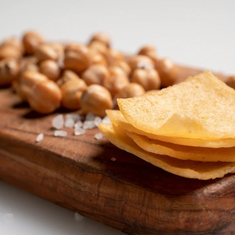 close up view of Peacasa chickpea chips on a cutting board with light sprinkle of salt and portion of chickpeas next to them