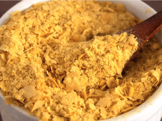 zoomed in image of nutritional yeast in a bowl with wooden spoon scooping some out