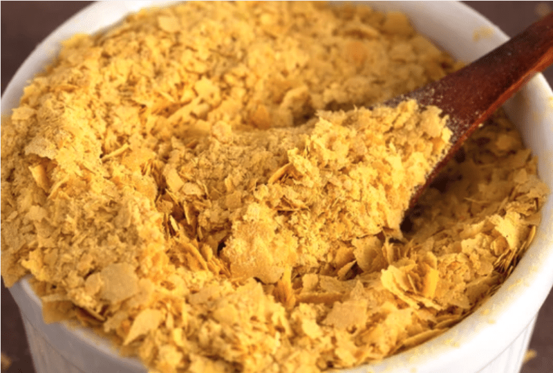 zoomed in image of nutritional yeast in a bowl with wooden spoon scooping some out